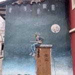 Street art of an electric guitarist wearing a traditional Cuenca headdress, playing on a building under a full moon